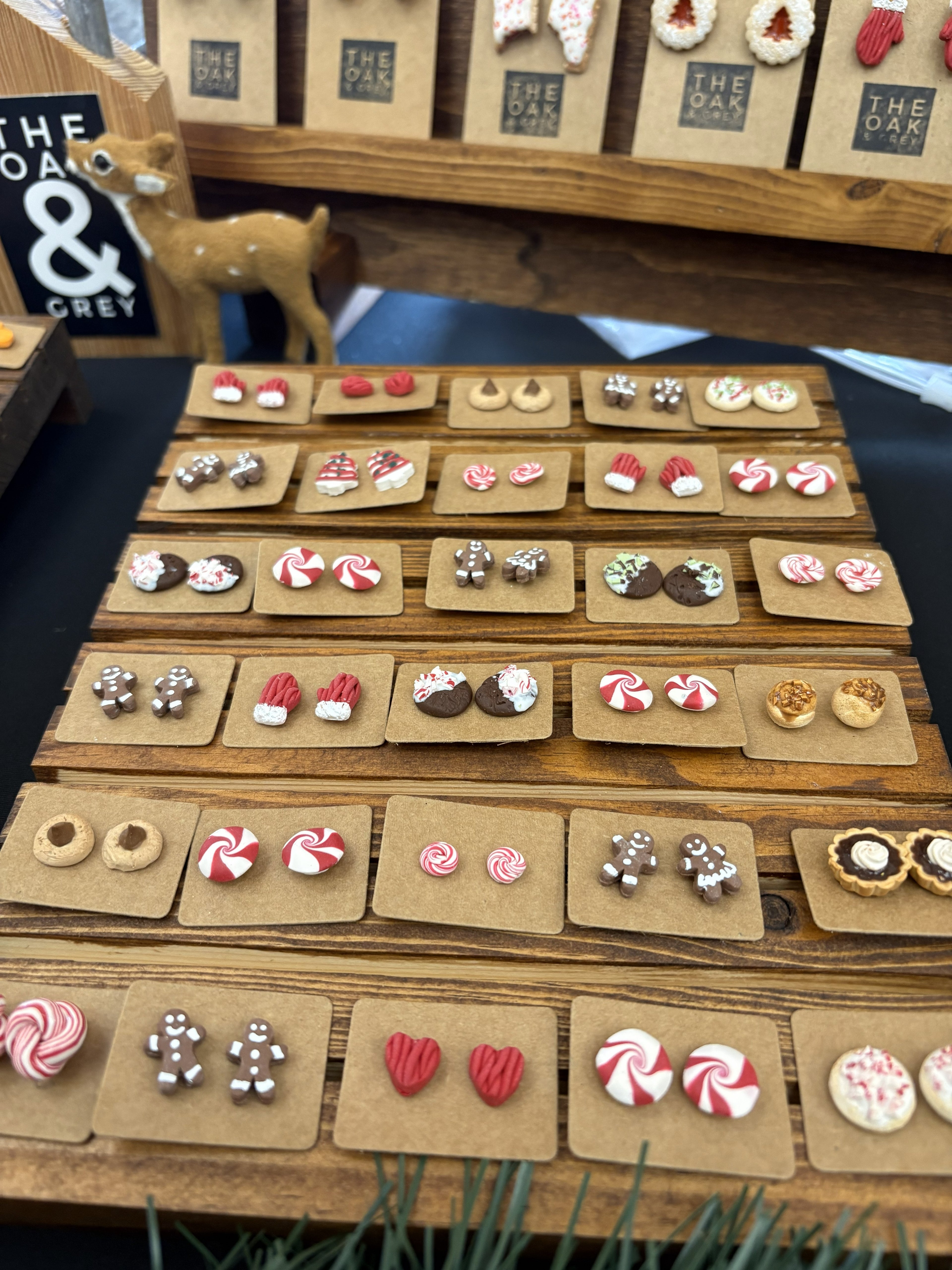 Display of various earrings on wooden trays with 'The Oak & Grey' branding.