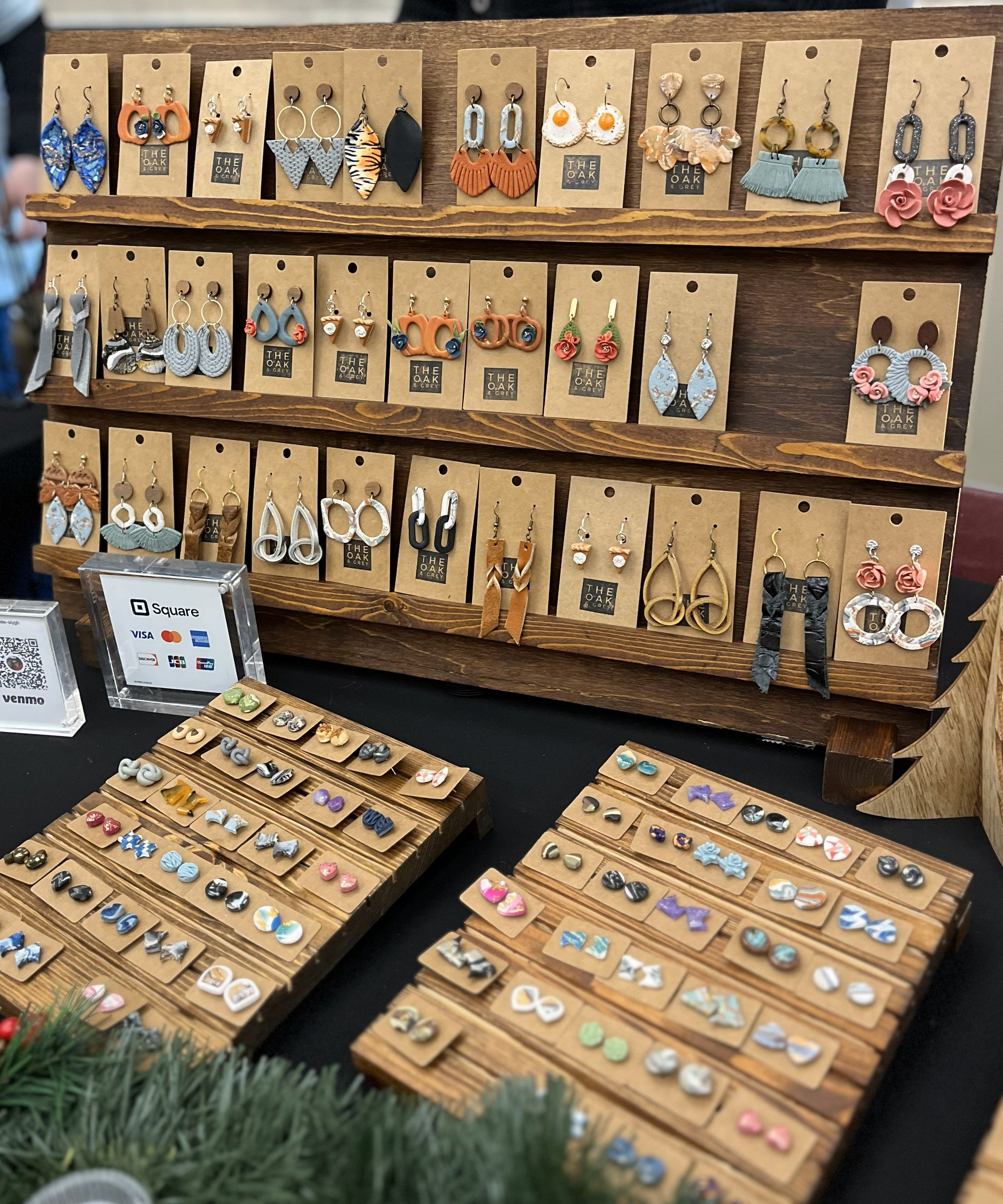 Wooden display rack with various earrings on cards, surrounded by additional earring sets.